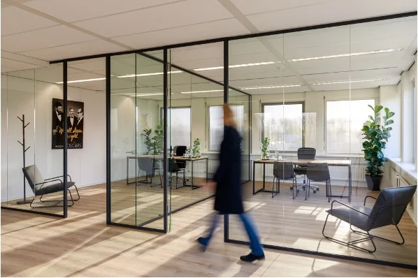 Moderne kantoorruimte aan de Baarnsche Dijk met glazen vergaderruimtes, designmeubilair en een persoon die voorbijloopt.